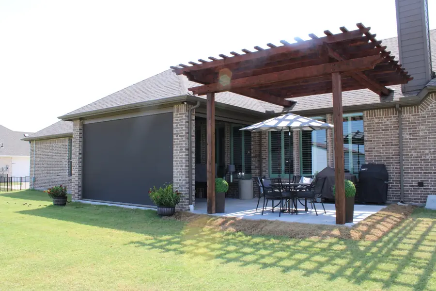 Cedar pergola with a motorized screen over a patio at the back of a brick home