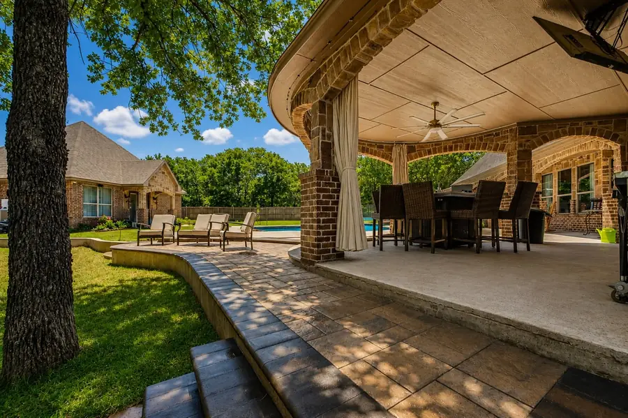 Covered patio and paver deck beside a pool under a mature oak in North Texas