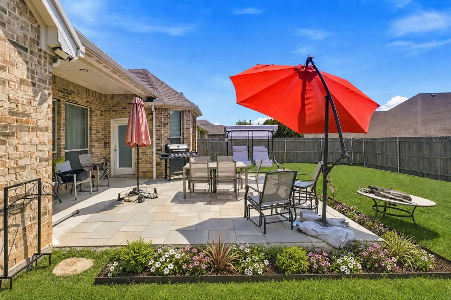Large-format stone patio with dining and lounge areas edged by a flower bed
